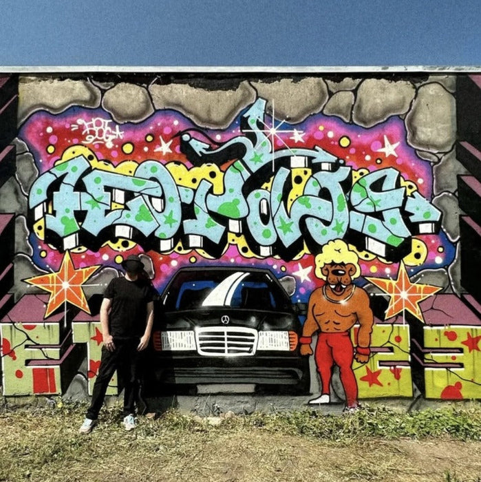 Person standing next to a car in front of a colorful graffiti mural on a wall.
